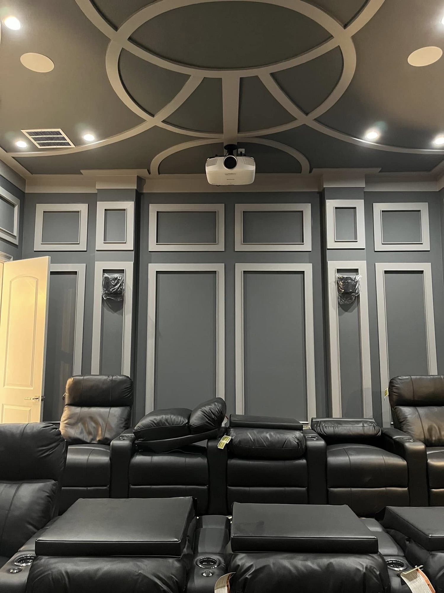 A home theater with leather riser seating beneath a decorative circular ceiling medallion and a ceiling mounted projector.